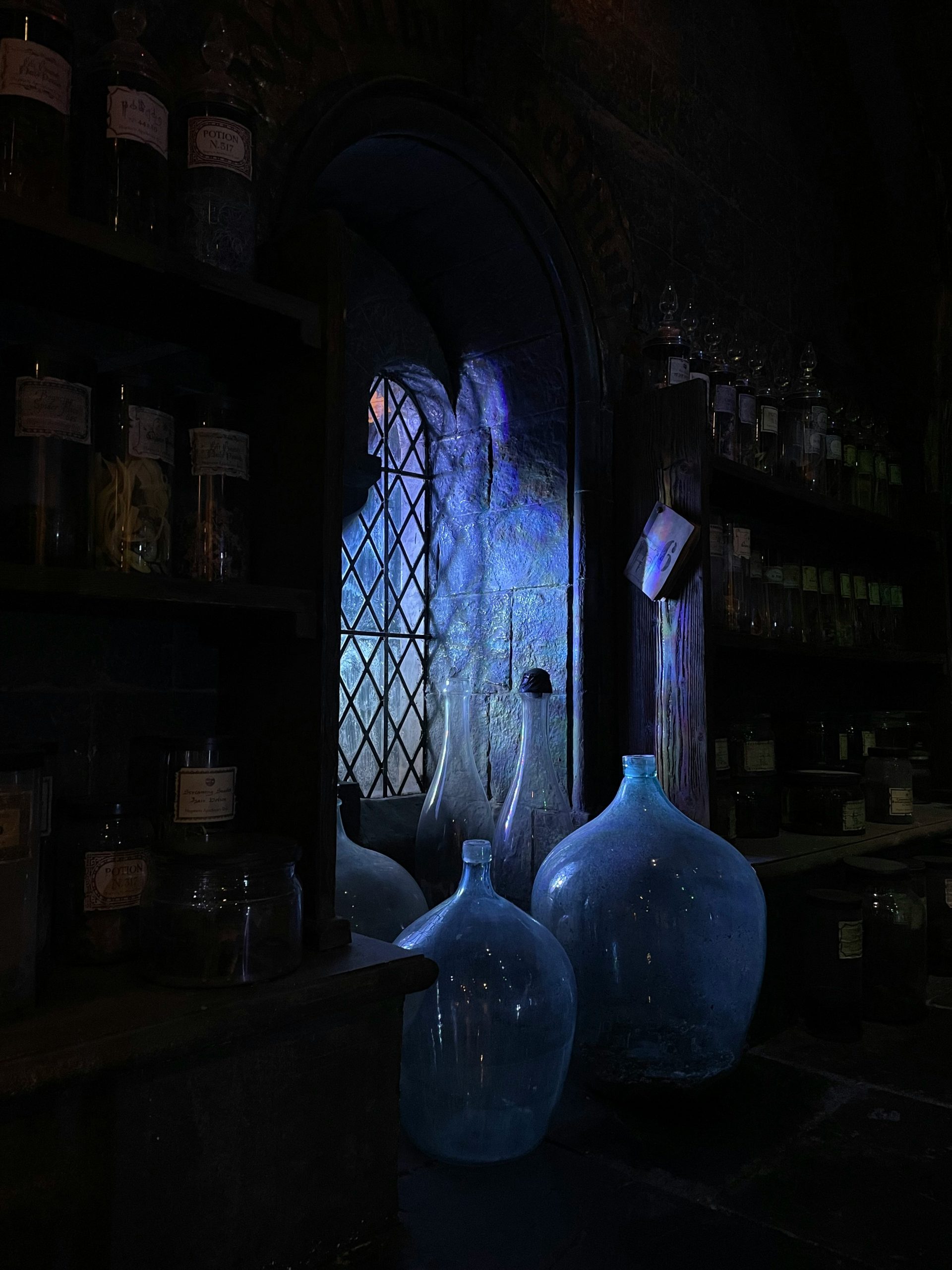 Glass bottles and apothecary jars glowing in blue light by an arched window