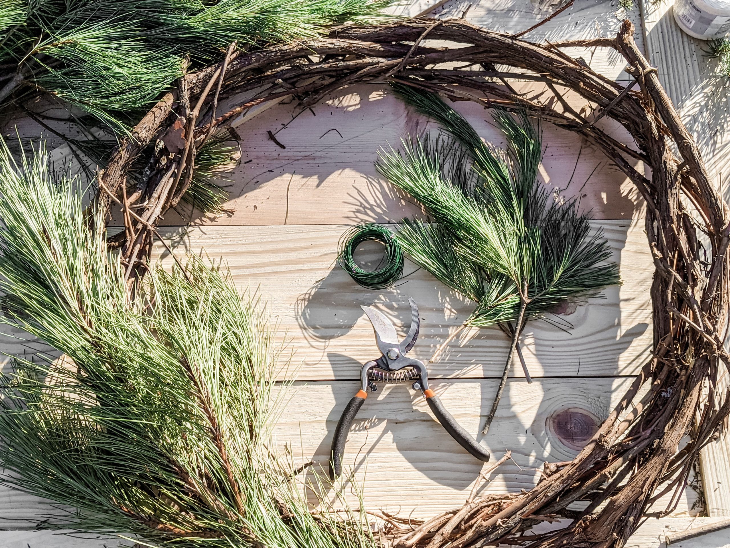 Grapevine wreath with pine boughs, floral wire and pruning shears on a wooden table
